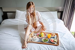 Young Smiling Beautiful Woman Having Breakfast in Bed in Cozy Hotel Room