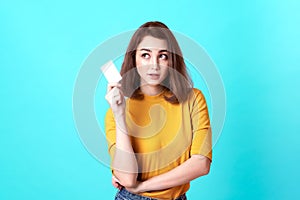 Young smiling beautiful woman in yellow shirt showing credit card in hand over blue background