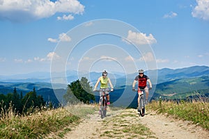 Young smiling bikers man and woman in professional sportswear riding bikes on dusty mountain road