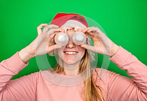 Young smiling blonde girl in a red winter Christmas Santa Claus hat holds Christmas decorative white balls in her hands near her