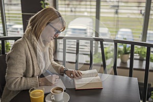 Young smiling woman in a restaurant reading a book and taking no