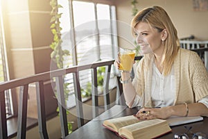Young smiling blonde woman in a restaurant reading a book and dr