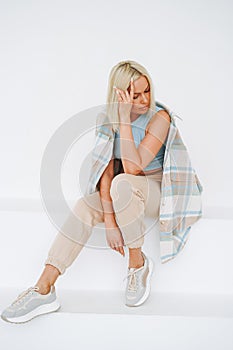 Young smiling blonde woman in sportswear sitting on background of white wall