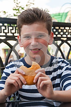 Young smiling boy with a fashionable hairstyle and a burger