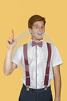 A young smiling boy teenager  proving something by raising her index finger up  against  yellow background in the studio