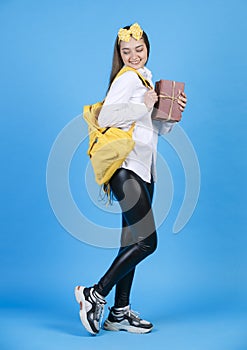 Young smiling brunette with bunch of books standing, shyly bending one leg, while looking back.