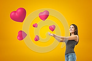 Young smiling brunette girl wearing casual jeans and t-shirt with palms up and pink hearts on yellow background