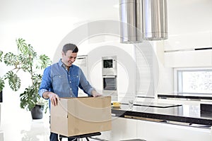 Young smiling brunette man unpacking box with kitchen tools at home