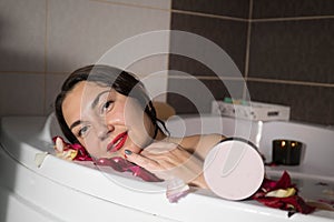 Young smiling brunette woman taking a bath with rose petals at home, doing spa treatments for balance and mental health..