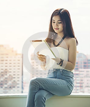 Young smiling business asian woman sitting near window and uses digital tablet