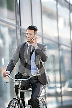 Young smiling business man with phone riding a bicycle