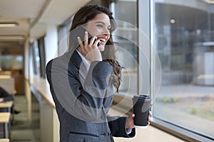 Young smiling business woman using smartphone near computer in office