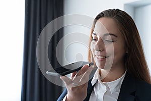 Young smiling business woman using vocal or voice activated digital assistant in smartphone