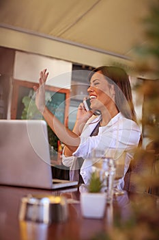 Young smiling business woman working in cafe and talking on smart phone. Girl appears to someone in the passage.