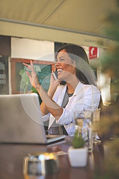 Young smiling business woman working in cafe and talking on smart phone. Girl appears to someone in the passage.