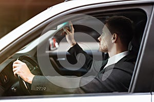 Young smiling businessman adjusting sunroof in his car before starting his trip , modern technologies concept