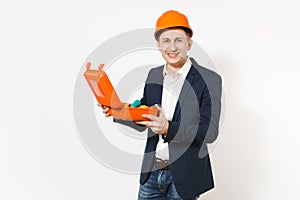 Young smiling businessman in dark suit, protective construction helmet holding opened case with instruments or toolbox