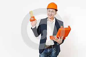 Young smiling businessman in dark suit, protective construction orange helmet holding opened case with instruments or