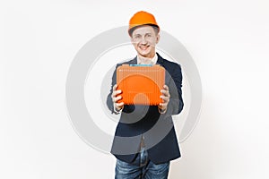 Young smiling businessman in dark suit, protective hardhat holding case with instruments or toolbox with copy space