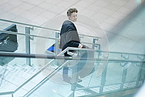 Young smiling businessman going down a stairway with his suitcase, lookin up