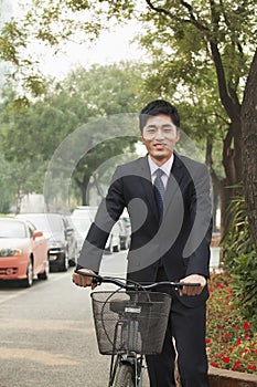 Young, smiling businessman holding a bicycle on a city street in Beijing, China