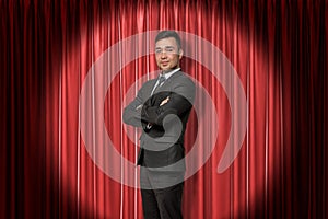 Young smiling businessman on red stage curtains background