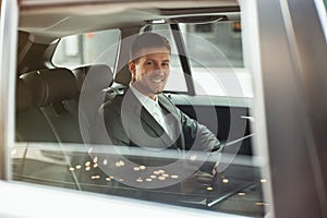 Young smiling businessman works in his laptop while sittingin his car on the way to meetting with partners, multitasking concept