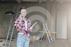 Young smiling businesswoman builder,engineer, architect,designer in workshop, talking on cell phone