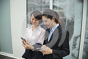 Young smiling businesswomen looking at their cell phones outside of the office building