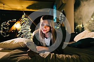Young smiling caucasian woman using mobile phone in holidays at home on the bed