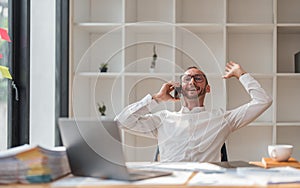 Young smiling cheerful happy entrepreneur in casual office making phone call while working with laptop