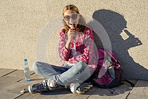 A young smiling cool girl, shod on roller skates, sits on the si