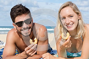 Young smiling couple eating biscuits on beach