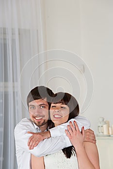 Young smiling couple embrace each other standing at home