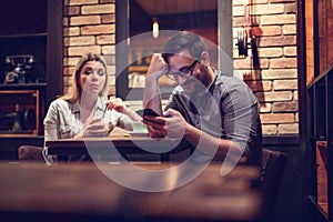 Young smiling couple in gorgeous restaurant. Man looking at phone. - Image