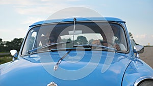 Young smiling couple in hats riding at vintage car during summer travel. Happy man and woman sitting at the front seat