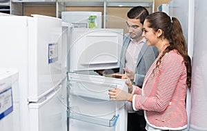 Young smiling couple looking at large fridges
