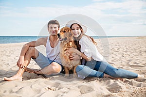 Young smiling couple in love sitting on beach with dog