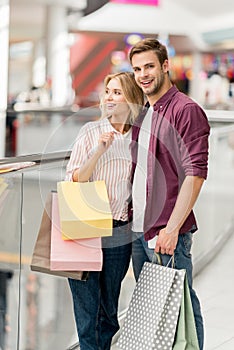 young smiling couple with shopping bags and smartphone at shopping