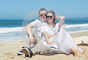 Young smiling couple in sunglasses sitting on the beach