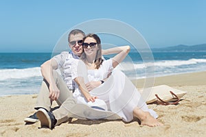 Young smiling couple in sunglasses sitting on the beach