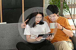 Young smiling couple using digital tablet while sitting on couch.