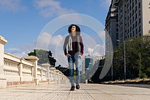 Young smiling curly haired latin man walking down a street on a sunny spring day. Low view angle