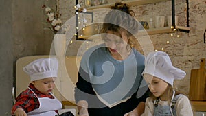 Young smiling curly mother with her son and daughter are cooking Christmas cookies at home in the cuisine with Xmas