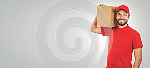 young smiling delivery man in red uniform and with shipment box on shoulder