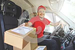 Young smiling delivery service man sitting in van and delivering boxes. giving package