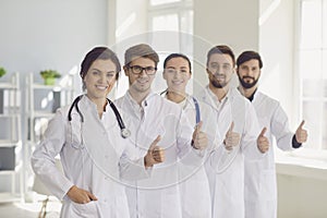 Young smiling doctors team portrait with thumbs up gesture in modern clinical hospital office.