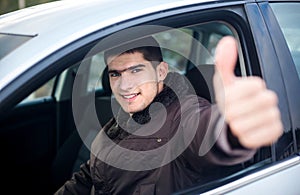 Young smiling driver thumb up in a car