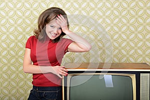 Young smiling ecstatic woman looking at camera in room with vintage wallpaper and retro TV set, retro stylization