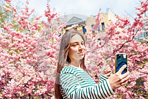 Young smiling european white female student taking selfie portrait with mobile phone. Making selfie woman on smartphone on cherry